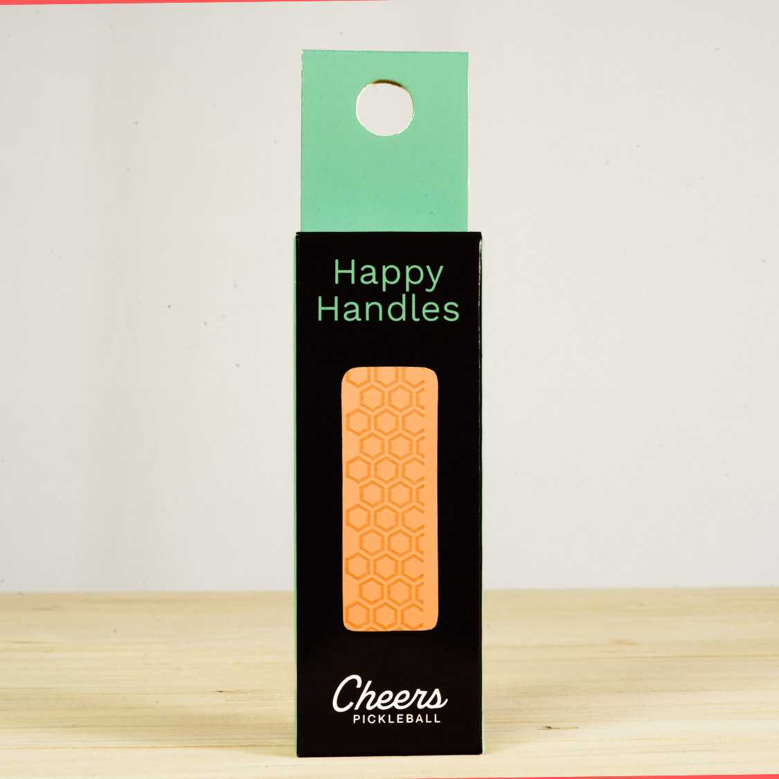 Happy Handles  Neon Orange Pickleball Grip in its packaging, featuring hexagon textured print, visible through the product box window