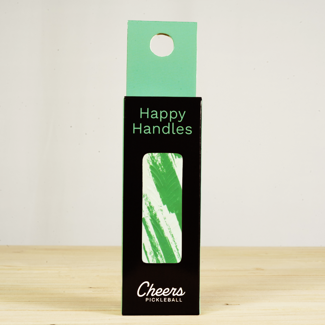 Happy Handles Brushed Green Pickleball Grip in its packaging, featuring green stripe marbling on white, visible through the product box window