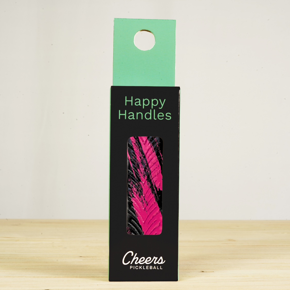 Happy Handles Brushed Pink Pickleball Grip in its packaging, featuring black stripe marbling on pink, visible through the product box window