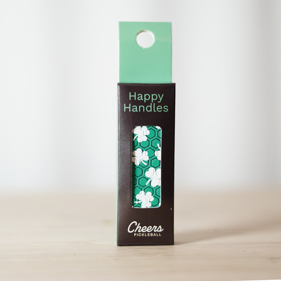 Happy Handles Lucky Clovers Pickleball Grip in its packaging, featuring clovers and leprechaun silhouette, visible through the product box window