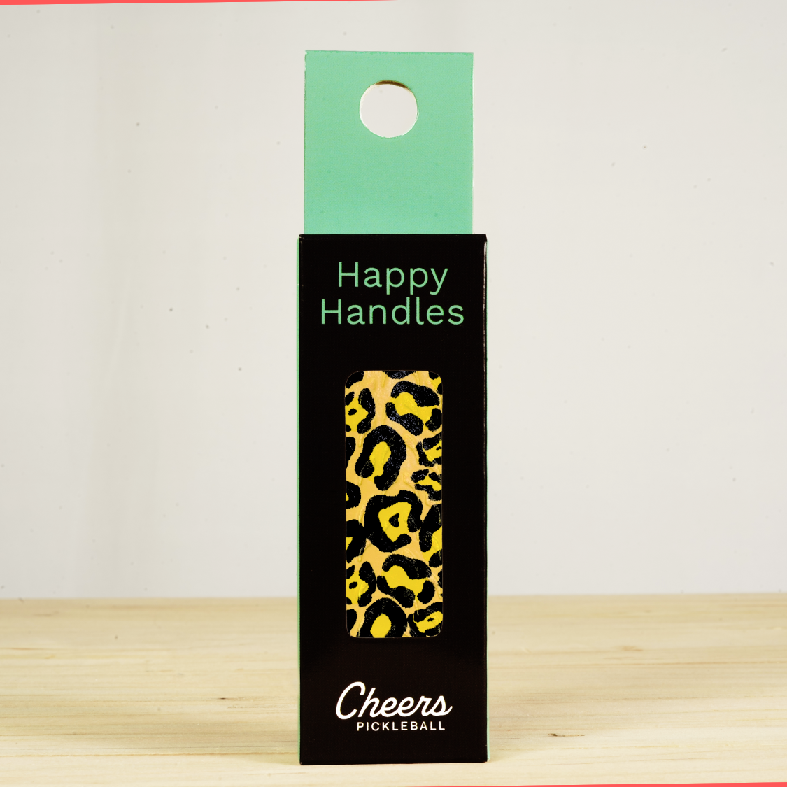 Happy Handles Leopard Pickleball Grip in its packaging, featuring a black and yellow leopard skin print, visible through the product box window
