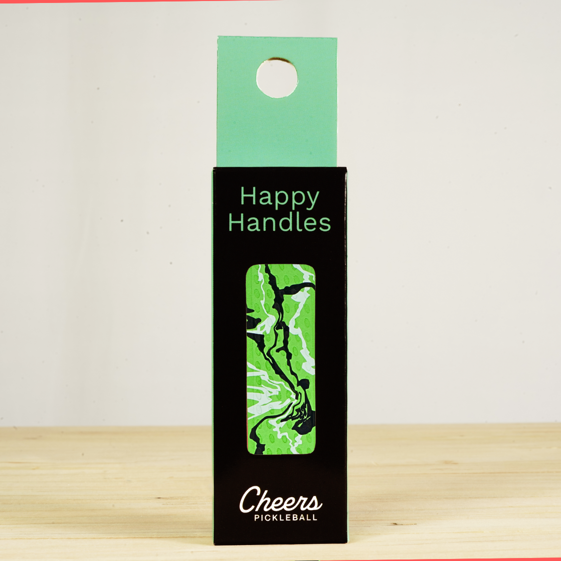 Happy Handles Paint Swirl, Green Pickleball Grip in its packaging, featuring white and black paint swirls, visible through the product box window