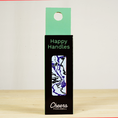 Happy Handles Paint Swirl, White Pickleball Grip in its packaging, featuring purple and black paint swirls, visible through the product box window